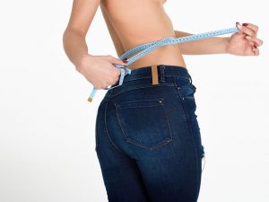 Young woman measuring waist with a tape. Fit and healthy girl with blue jeans on white background.