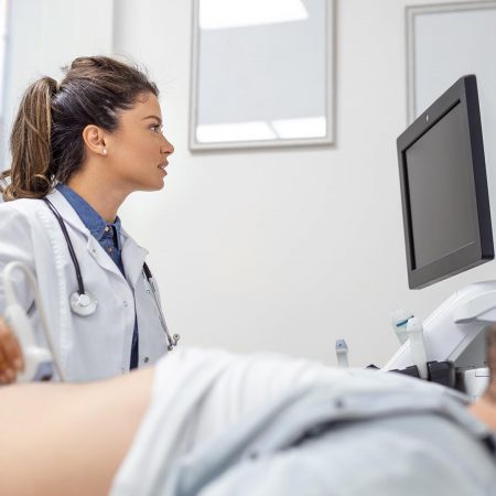 Careful female doctor in white coat sitting in front of an ultrasound apparatus and conducting abdominal diagnostics with transducer